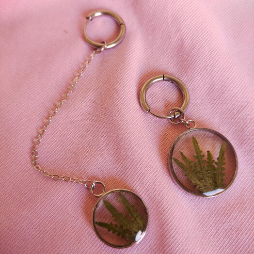 Asymmetrical earrings featuring a fern