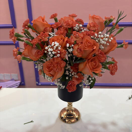 Des roses et des œillets orange dans un vase noir.